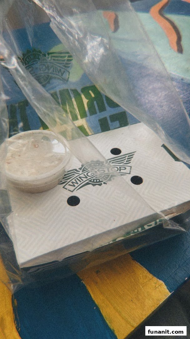 Wingstop packaging with a sauce cup, wrapped in plastic, on a patterned surface.
