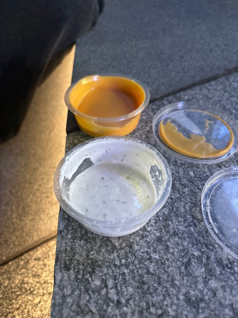 Close-up of two Wingstop dipping sauces in plastic containers on a stone surface.
