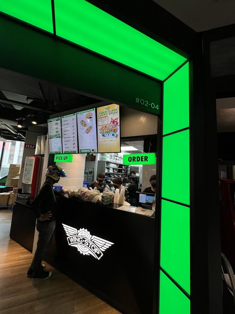 A customer at the Wingstop Funan counter, with digital menu boards and staff preparing orders.