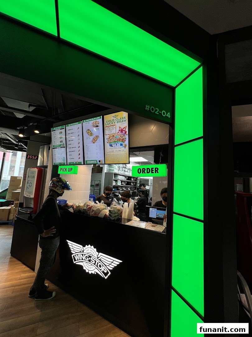 A customer at the Wingstop Funan counter, with digital menu boards and staff preparing orders.