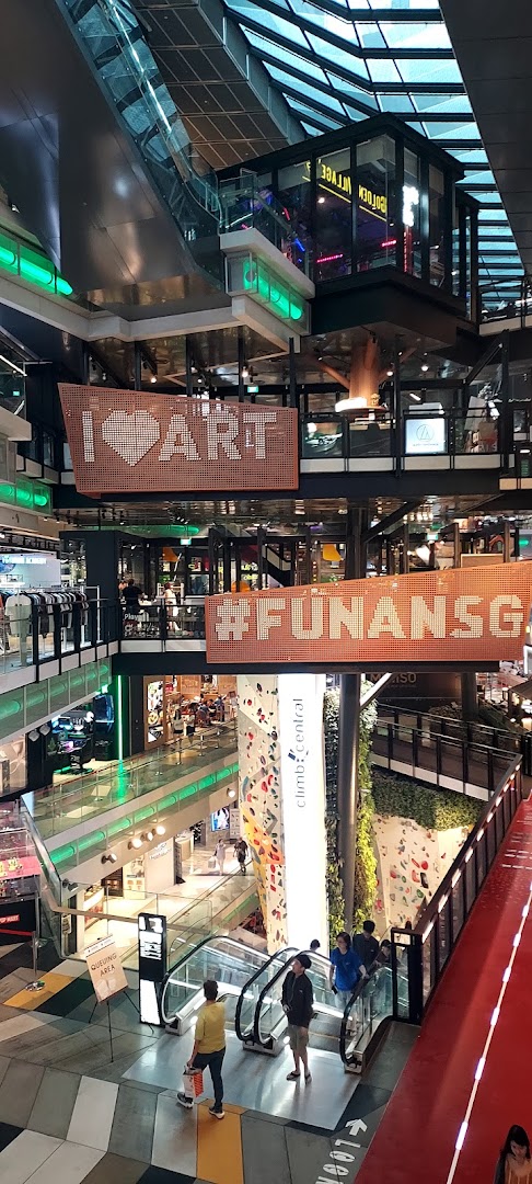 A vibrant multi-level view of Funan mall's interior, featuring escalators, a climbing wall, and artistic signage.