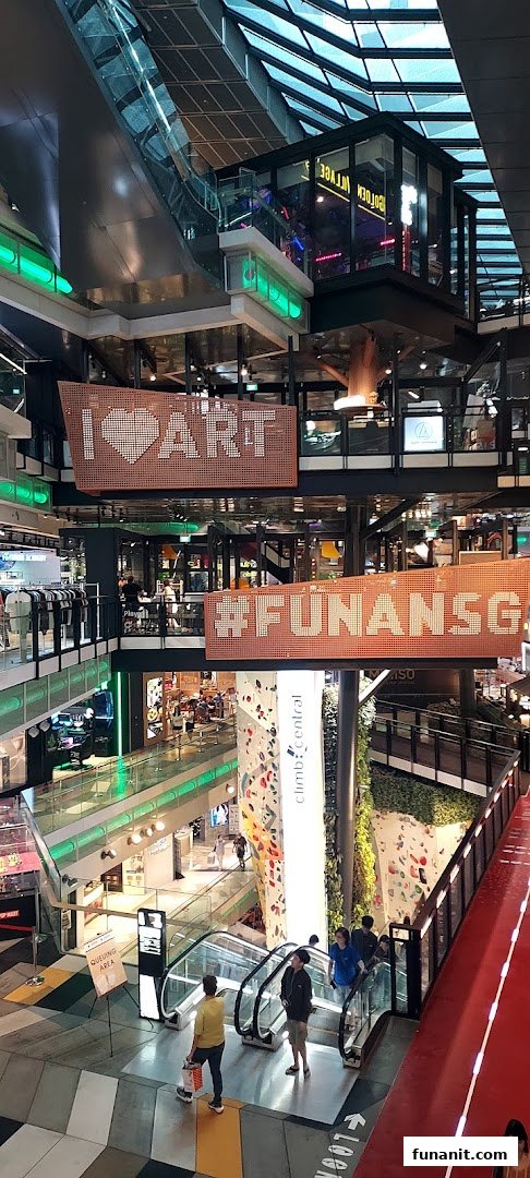 A vibrant multi-level view of Funan mall's interior, featuring escalators, a climbing wall, and artistic signage.