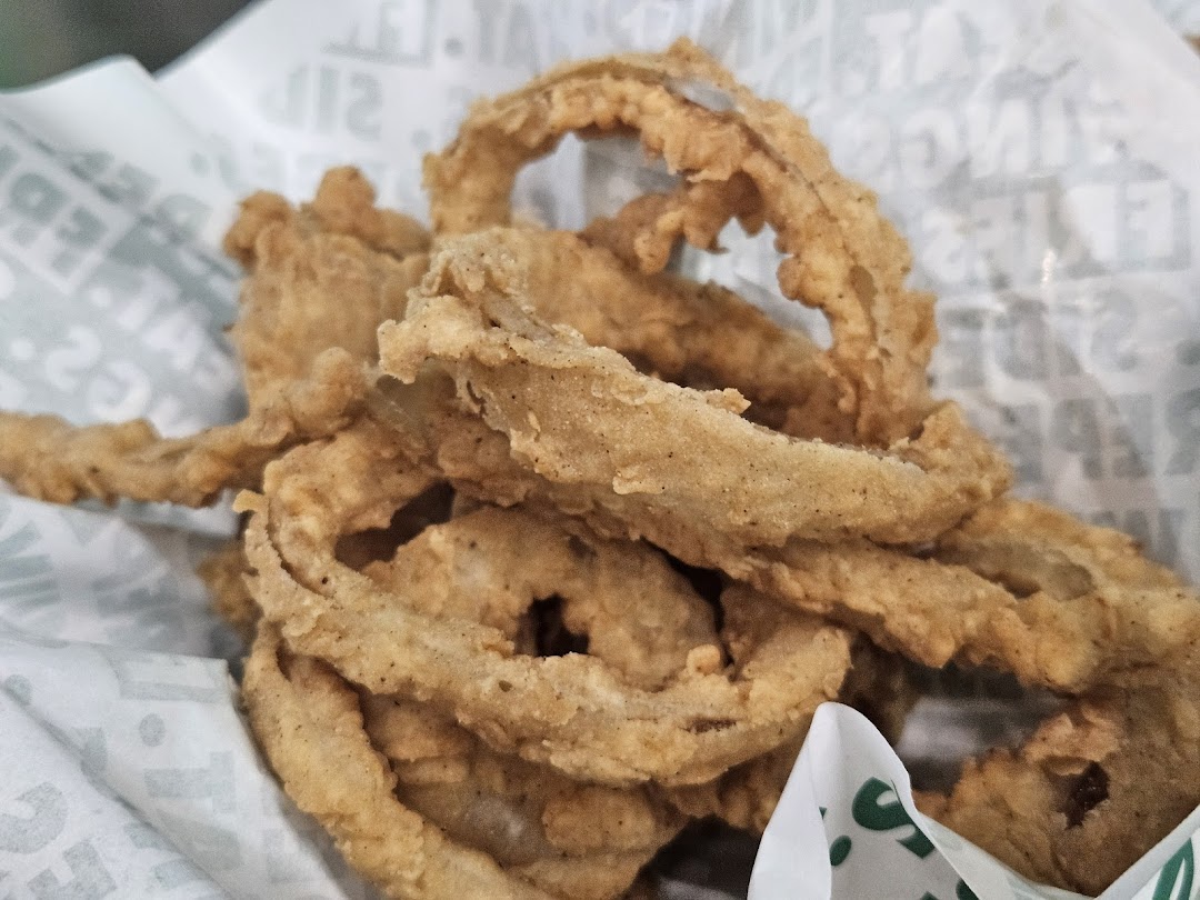 A close-up of crispy, golden-brown onion rings from Wingstop, served in branded paper.