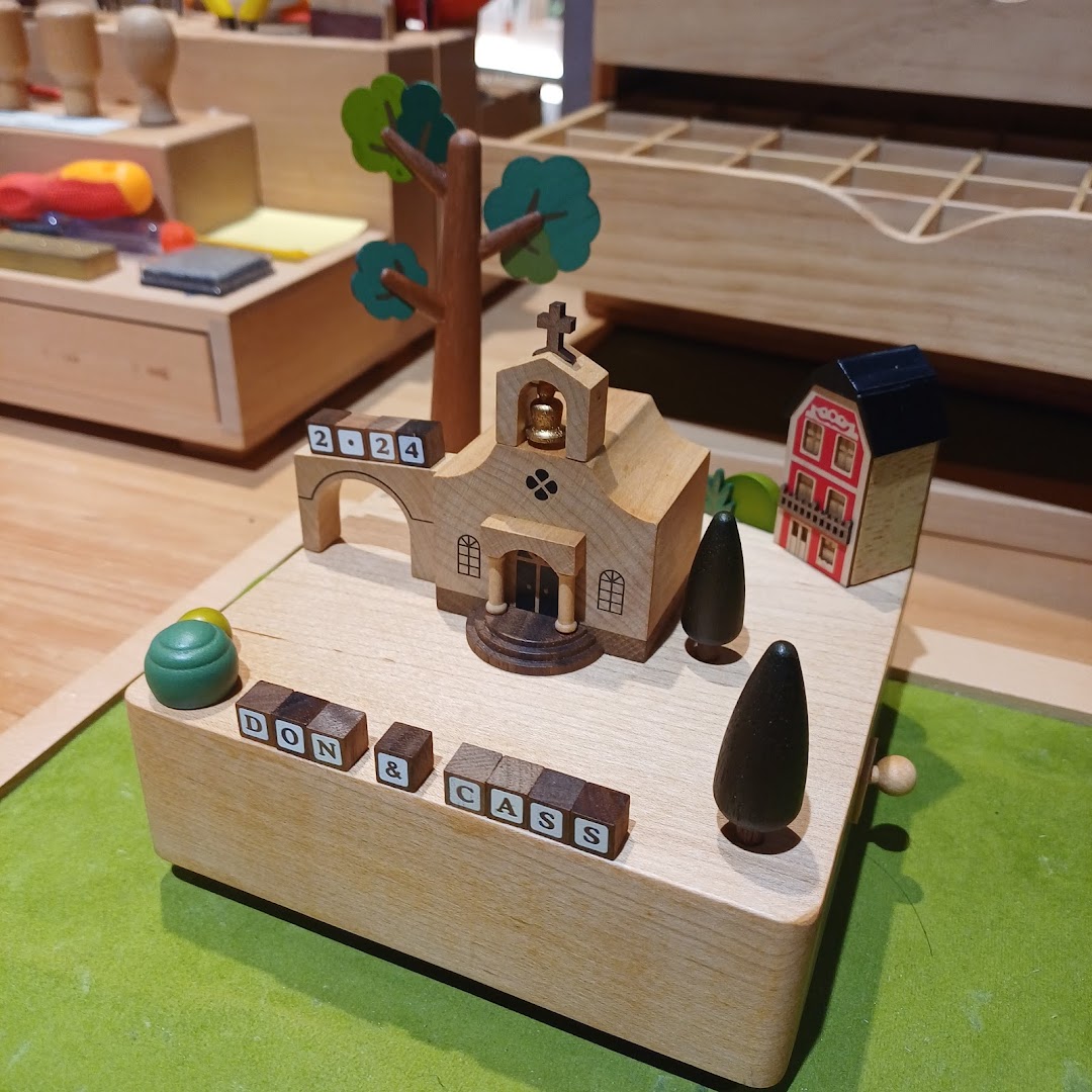 A beautifully crafted wooden music box featuring a church, trees, and personalized name blocks 'DON & CASS'.