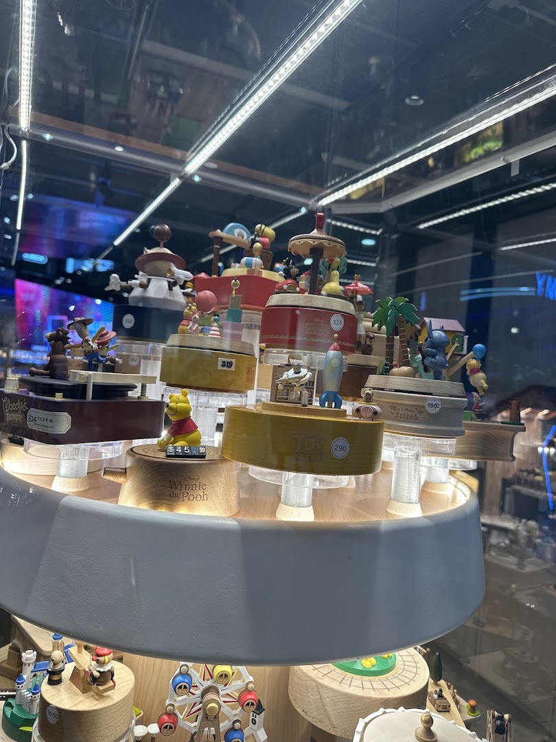 A display of intricately crafted wooden music boxes and figurines, including Winnie the Pooh, in a brightly lit retail case.