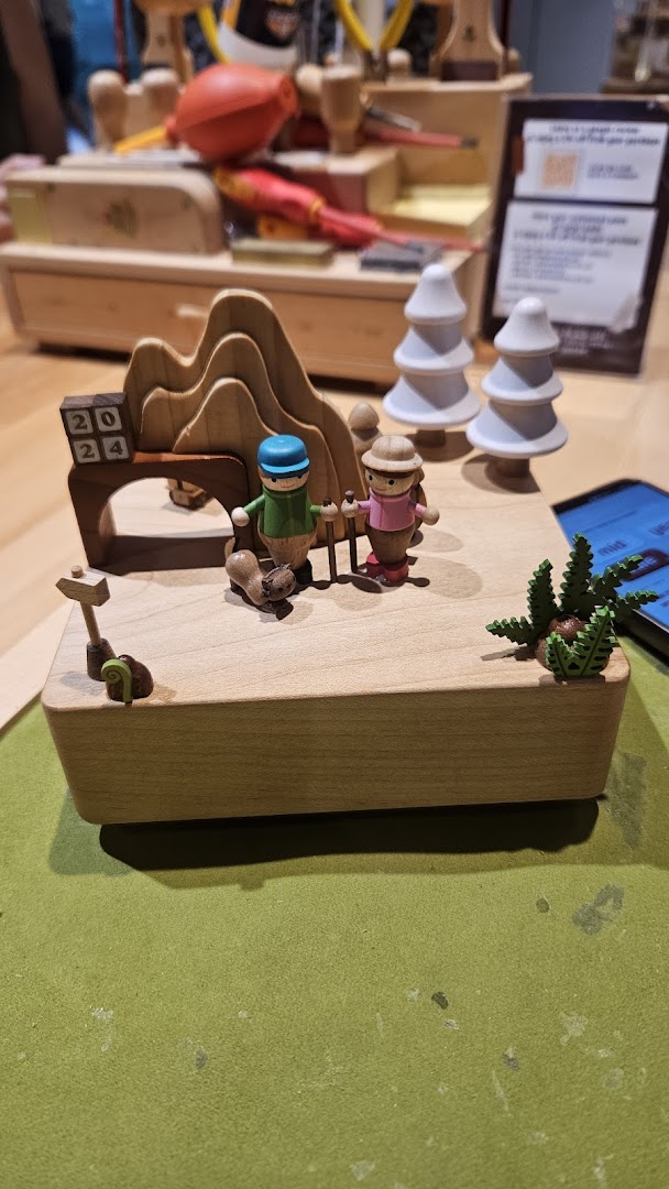 A detailed wooden music box featuring hikers, trees, and mountains, with a '2024' sign.