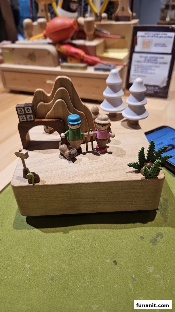 A detailed wooden music box featuring hikers, trees, and mountains, with a '2024' sign.