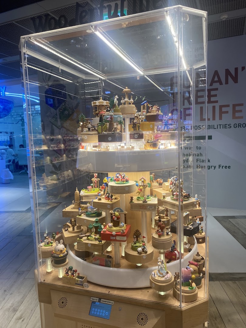 A clear display case showcasing a variety of intricate wooden music boxes and charming figurines from Wooderful Life.