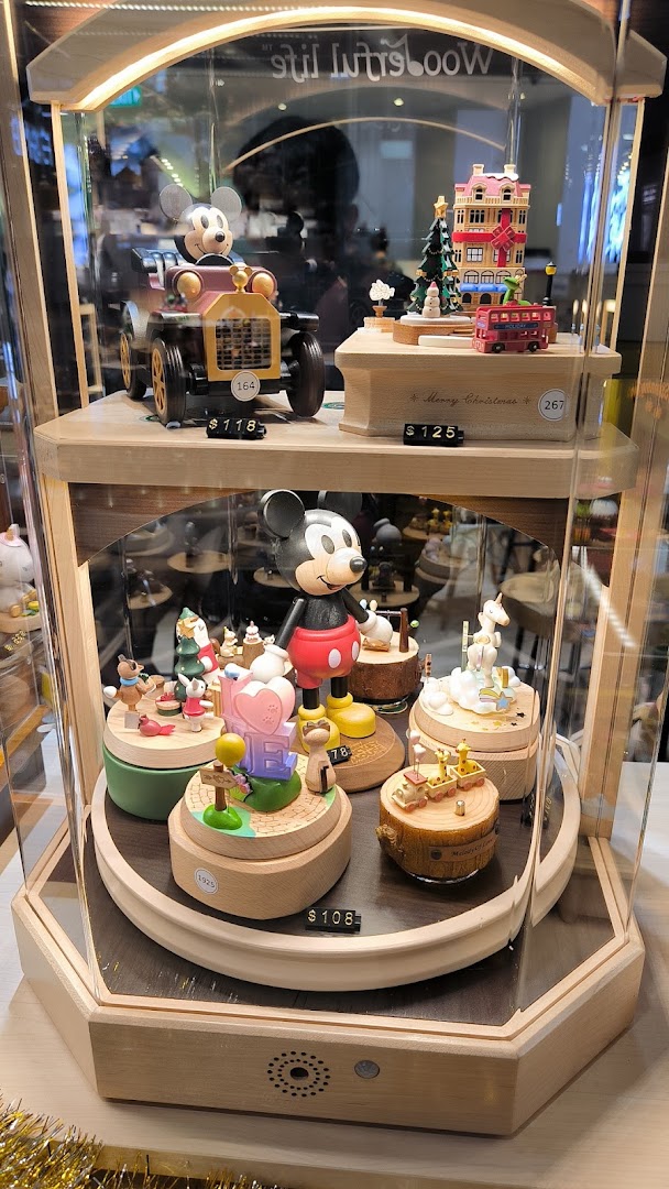 A display case showcasing intricate wooden music boxes and figurines, including Disney characters, with prices visible.