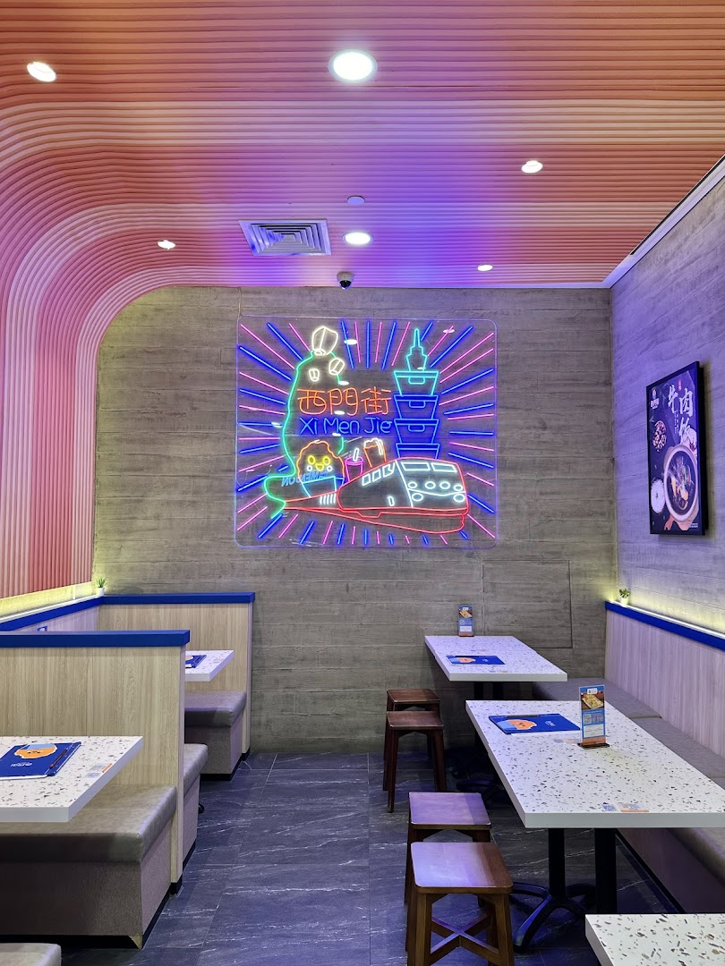 Vibrant interior of Xi Men Jie with a large neon sign, modern seating, and a cozy ambiance.