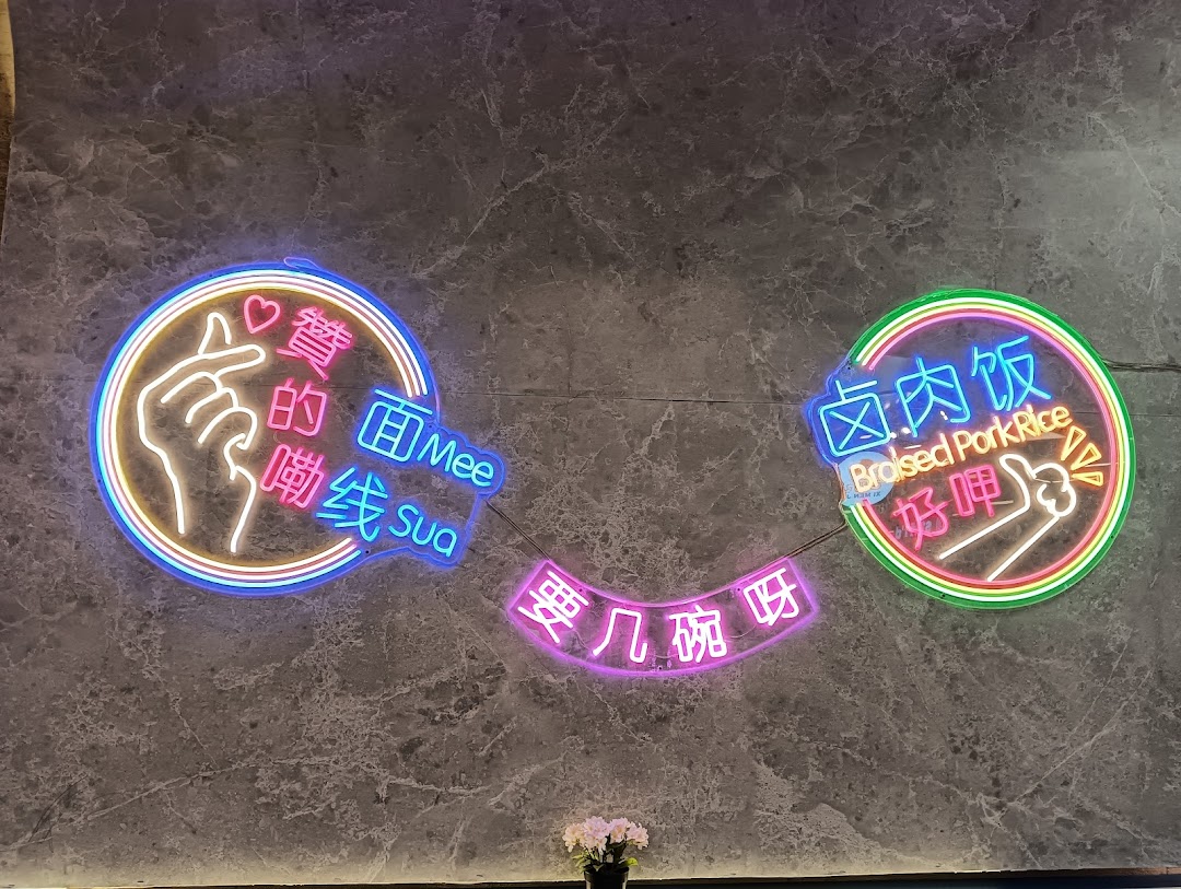 Vibrant neon signs on a grey wall promoting Mee Sua and Braised Pork Rice with playful hand gestures.