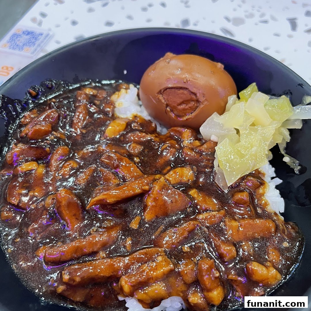 A close-up of a delicious bowl of Taiwanese braised pork rice (Lu Rou Fan) with a braised egg and pickled vegetables.