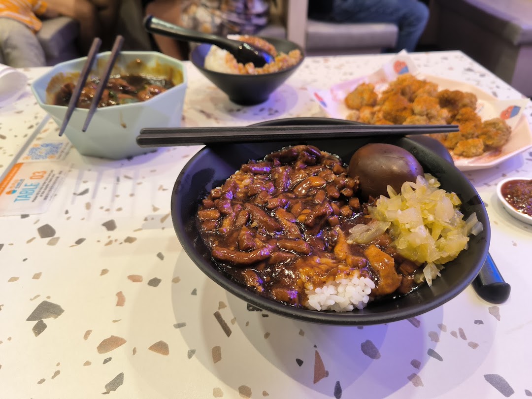 A close-up of delicious Taiwanese braised pork rice, pickled vegetables, and other dishes on a speckled table.