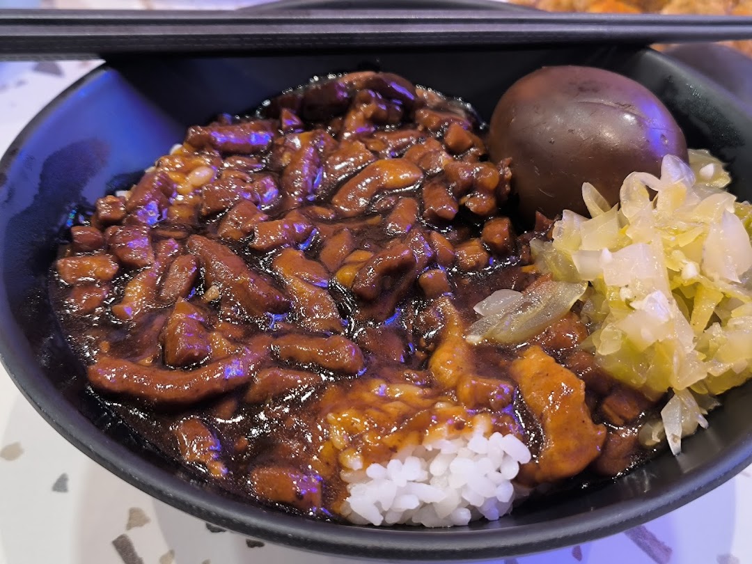 A close-up of a delicious bowl of Taiwanese braised pork rice (Lu Rou Fan) with a braised egg and pickled vegetables.