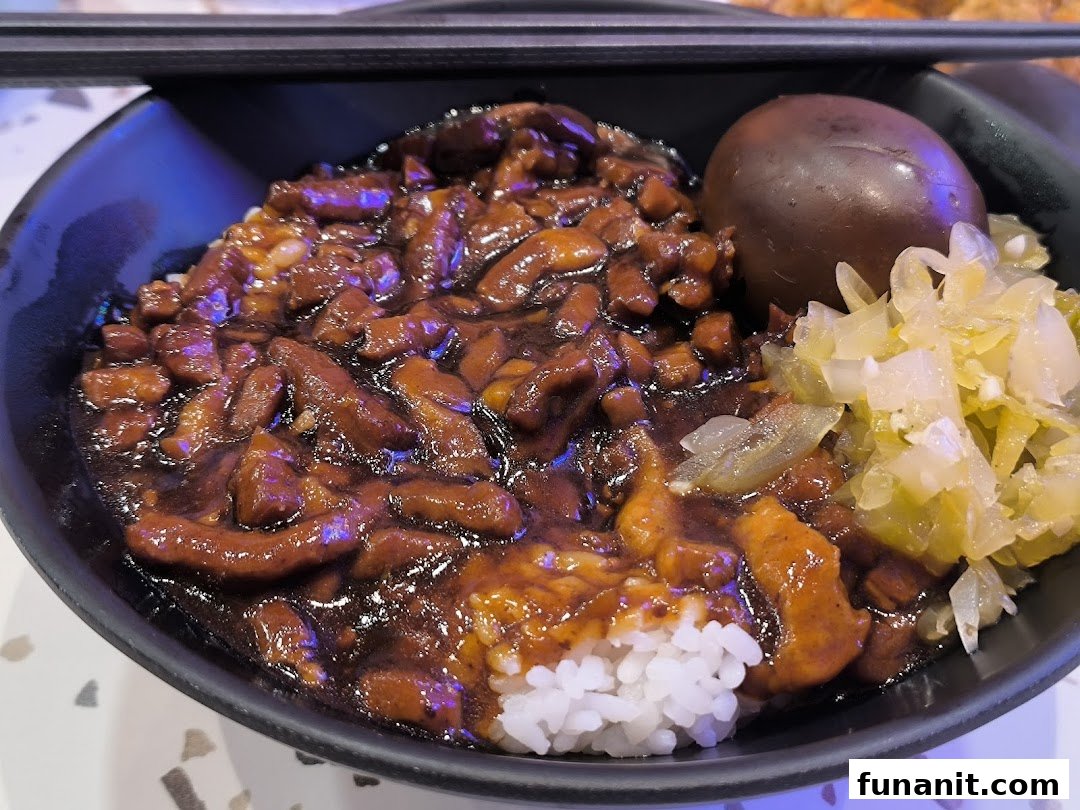 A close-up of a delicious bowl of Taiwanese braised pork rice (Lu Rou Fan) with a braised egg and pickled vegetables.