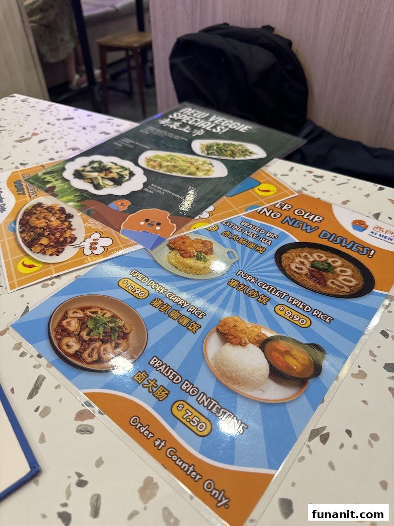 Close-up of laminated menu cards displaying various Taiwanese dishes and their prices on a speckled table.