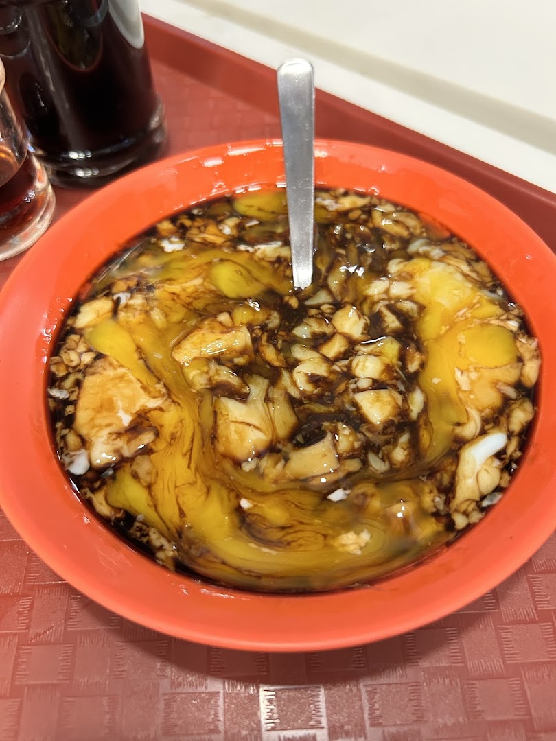 A close-up of soft-boiled eggs with dark soy sauce and pepper in an orange bowl, a classic Ya Kun dish.