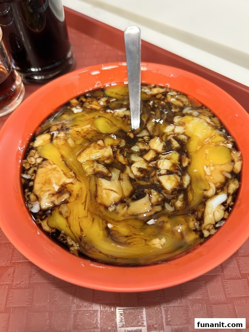 A close-up of soft-boiled eggs with dark soy sauce and pepper in an orange bowl, a classic Ya Kun dish.