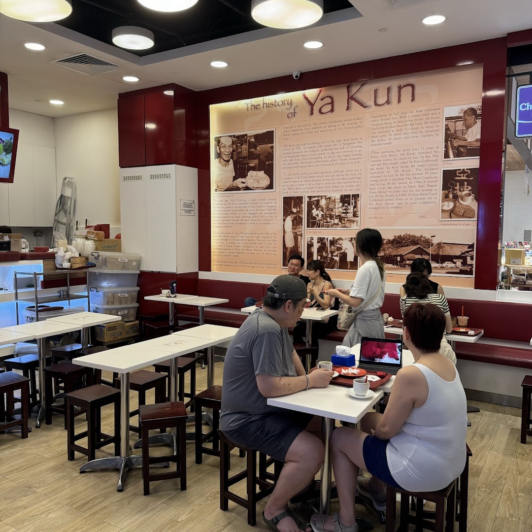 Customers enjoy traditional kaya toast and coffee in the cozy interior of Ya Kun Kaya Toast, featuring a historical wall display.