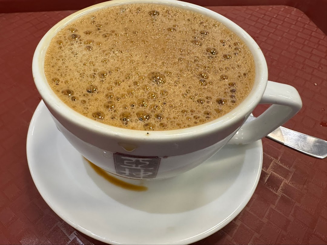 A close-up of a frothy beverage in a white cup with the Ya Kun Kaya Toast logo on a red tray.