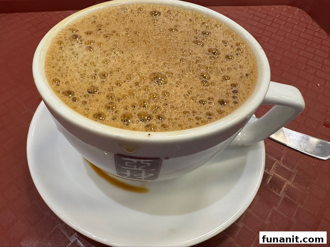 A close-up of a frothy beverage in a white cup with the Ya Kun Kaya Toast logo on a red tray.