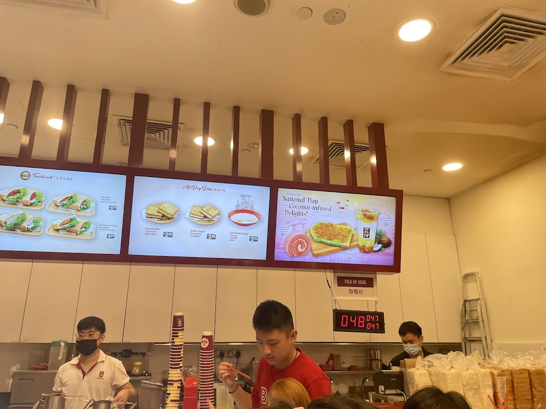 A bustling Ya Kun Kaya Toast counter showcasing various menu boards with toast, sides, and special drinks.