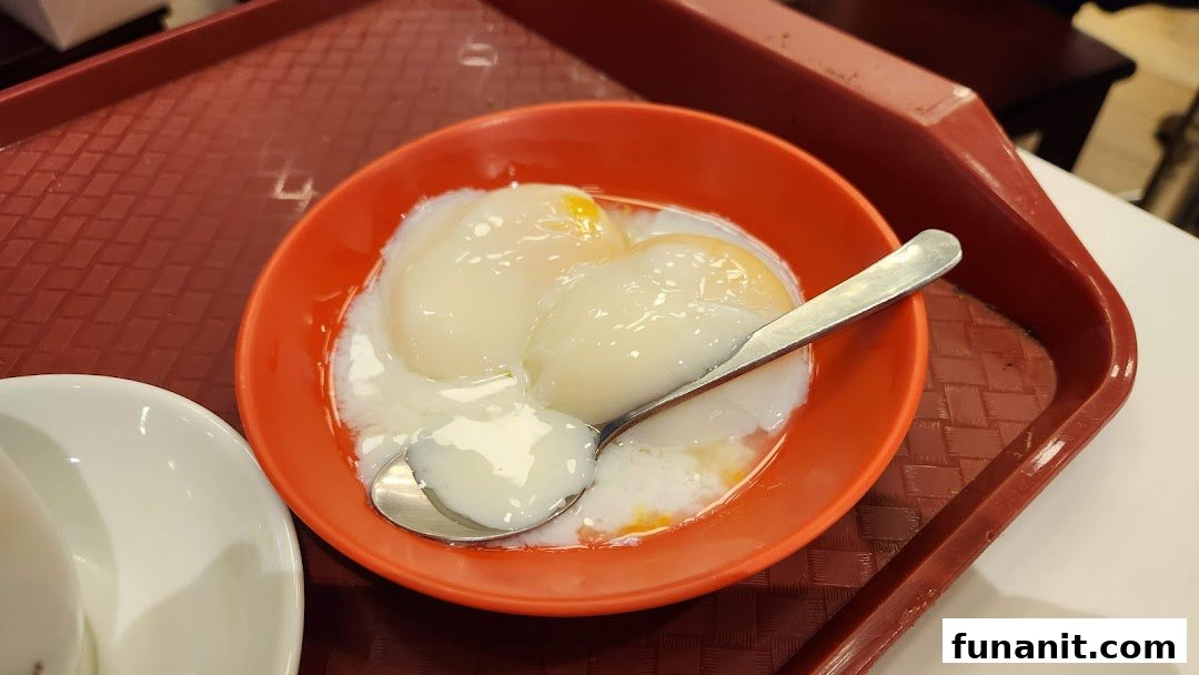A close-up of two perfectly soft-boiled eggs in an orange bowl on a red tray.