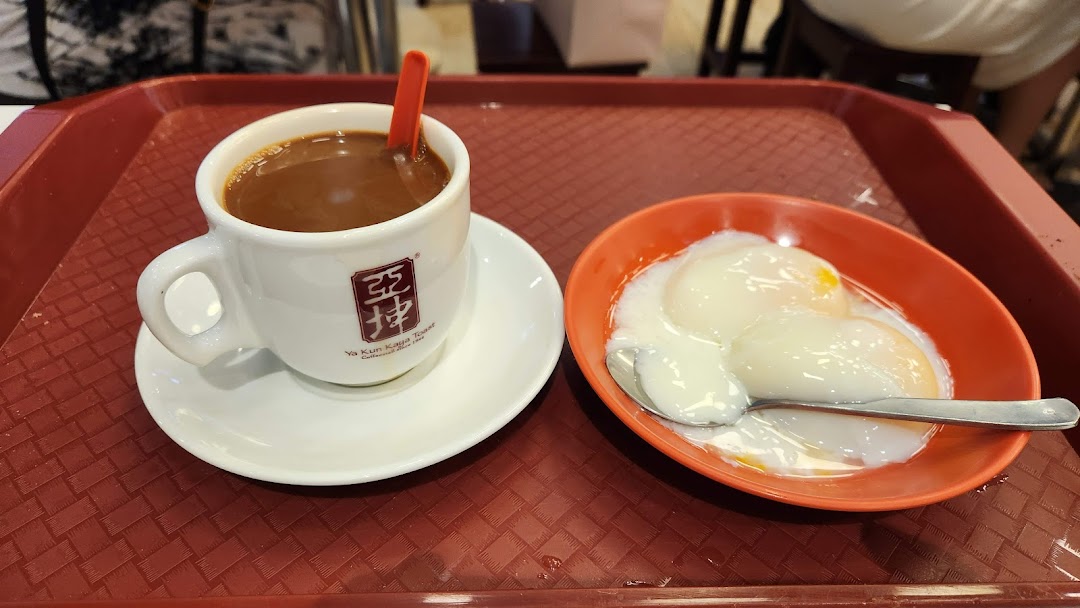 A traditional Singaporean breakfast set featuring a cup of coffee and soft-boiled eggs on a red tray.