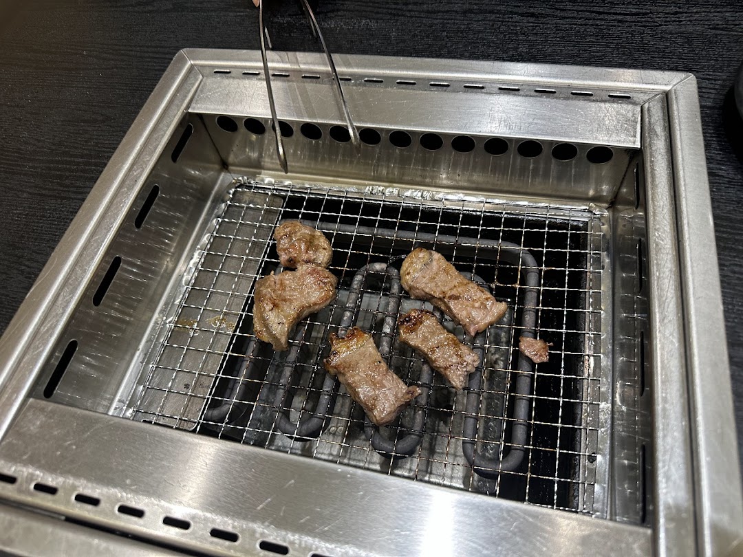 Close-up of delicious yakiniku meat grilling on a built-in tabletop grill with tongs.