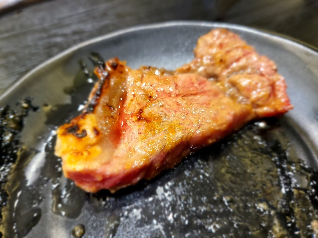 A close-up of a perfectly grilled piece of yakiniku beef on a dark plate.