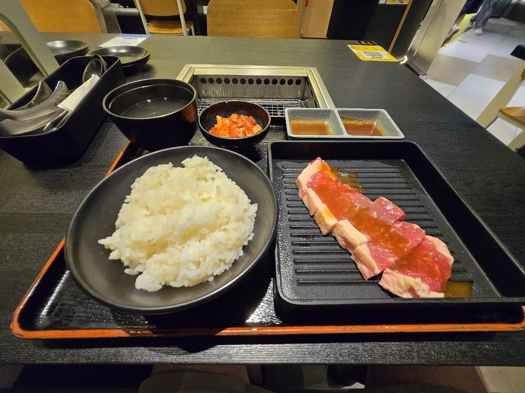 A yakiniku meal set featuring raw meat, rice, soup, kimchi, and sauces on a table with a built-in grill.
