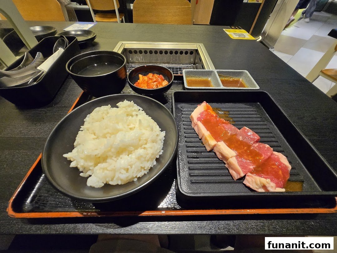 A yakiniku meal set featuring raw meat, rice, soup, kimchi, and sauces on a table with a built-in grill.