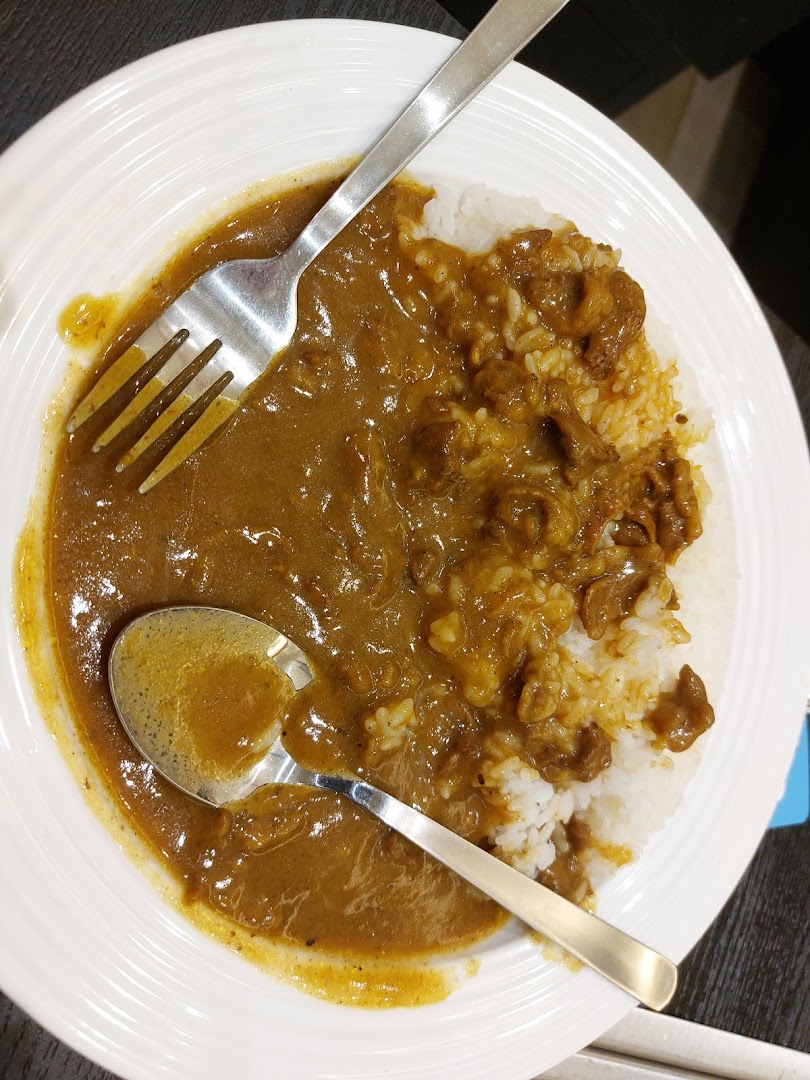 A close-up view of a plate of Japanese curry rice with meat, served with a fork and spoon.
