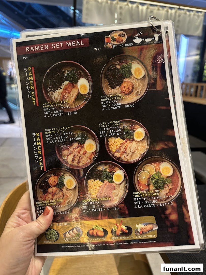 A hand holding a laminated menu displaying various ramen set meals and side dishes.