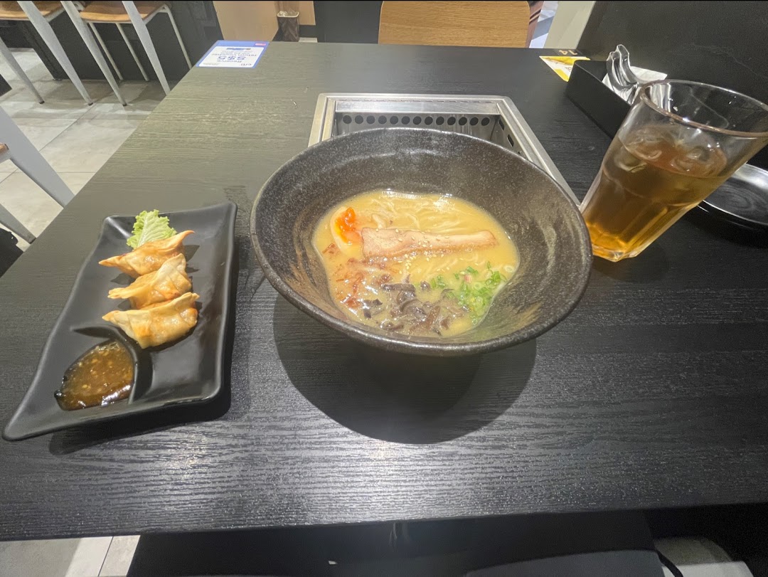 A delicious bowl of ramen and gyoza served on a black table with a refreshing drink.