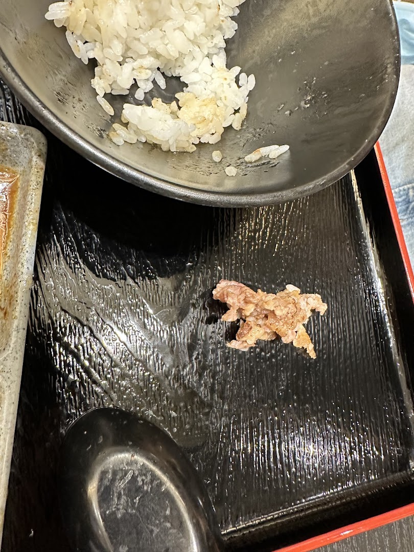 A close-up of a meal at Yakiniku Shokudo, featuring rice and a piece of grilled meat on a black tray.