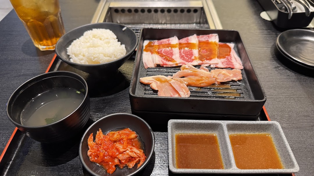 A delicious yakiniku meal set with raw beef, chicken, rice, soup, kimchi, and sauces on a black tray.