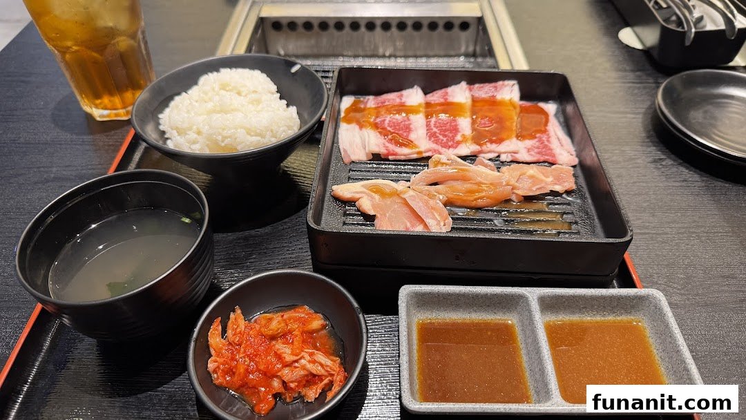 A delicious yakiniku meal set with raw beef, chicken, rice, soup, kimchi, and sauces on a black tray.