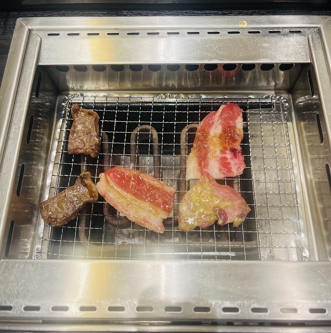 Various cuts of fresh yakiniku meat sizzling on a built-in tabletop grill at Yakiniku Shokudo.