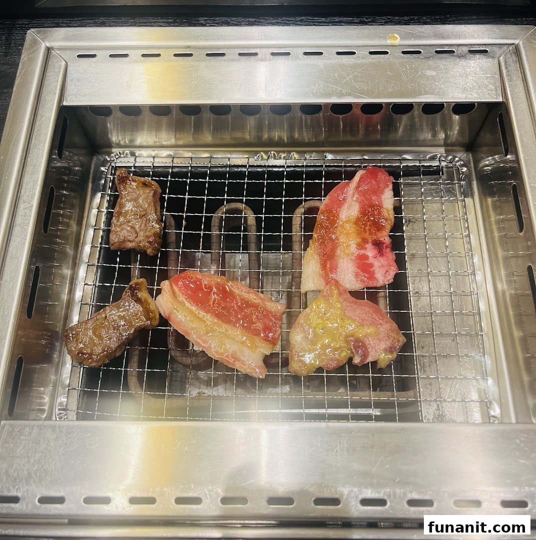 Various cuts of fresh yakiniku meat sizzling on a built-in tabletop grill at Yakiniku Shokudo.