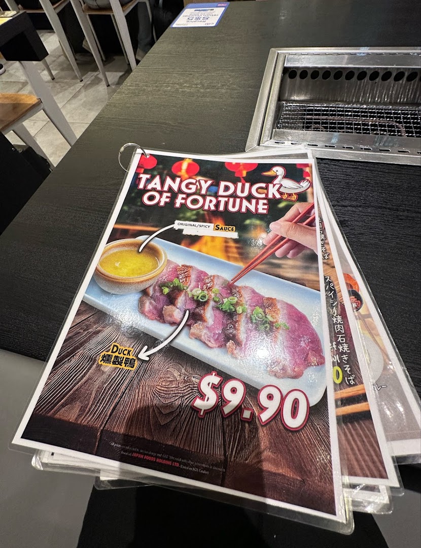 A close-up of a menu page featuring 'Tangy Duck of Fortune' with its price, on a restaurant table.