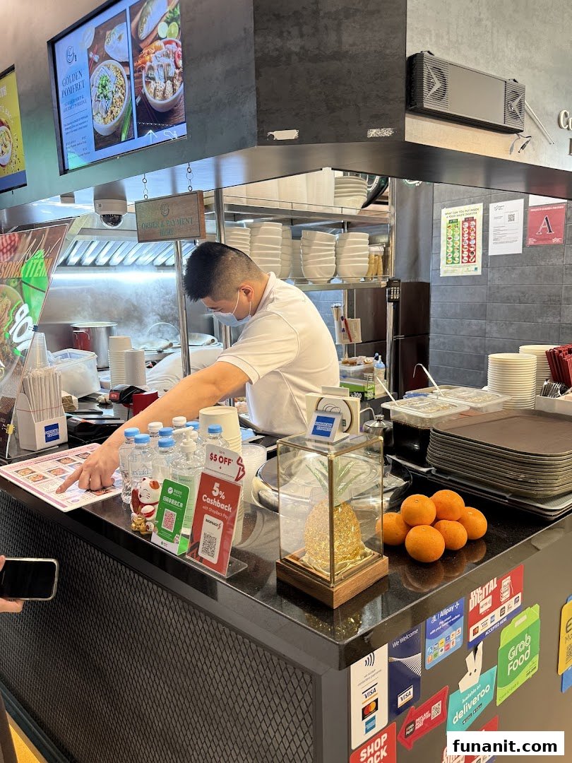 A chef prepares food behind a counter at Yan Ji Gourmet Seafood Soup, with a digital menu and payment options visible.