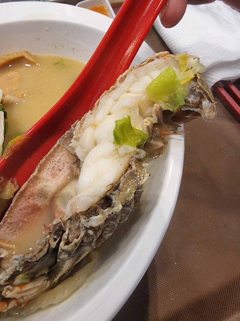 Close-up of a succulent mantis shrimp in a bowl of gourmet seafood soup, held by a red spoon.