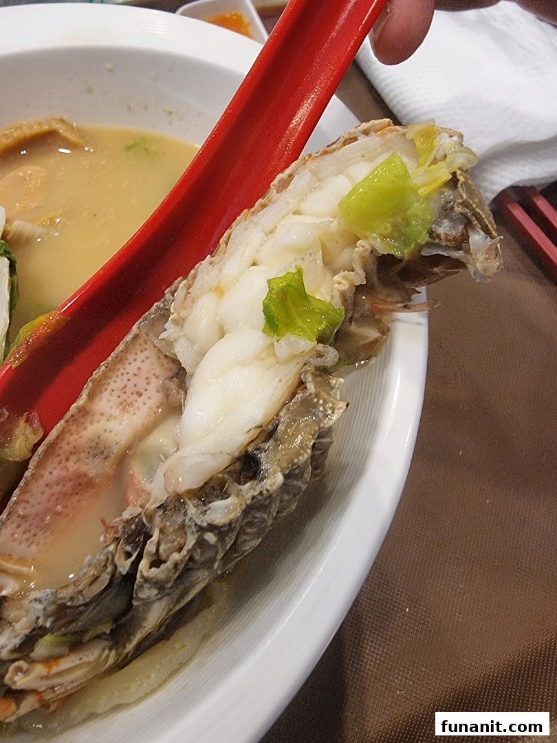 Close-up of a succulent mantis shrimp in a bowl of gourmet seafood soup, held by a red spoon.