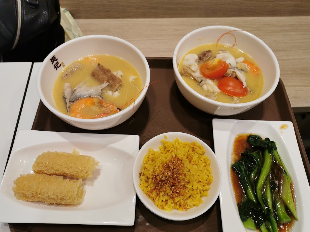 Two bowls of seafood soup with sides of rice, vegetables, and crispy fried items on a tray.