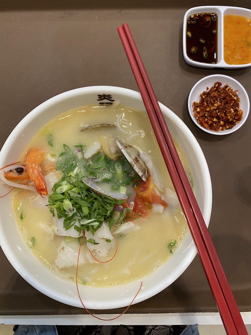 A close-up of a delicious bowl of seafood soup with prawns, fish, clams, and fresh greens.