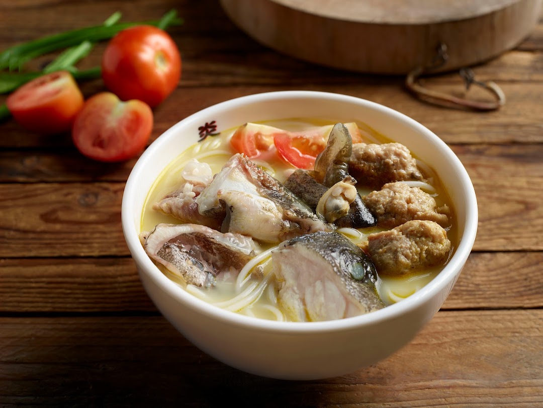 A close-up of a hearty bowl of seafood soup with fish slices, meatballs, and tomatoes.