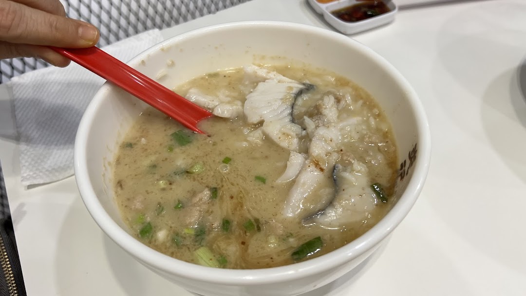 A close-up of a bowl of seafood soup with fish slices and a red spoon.