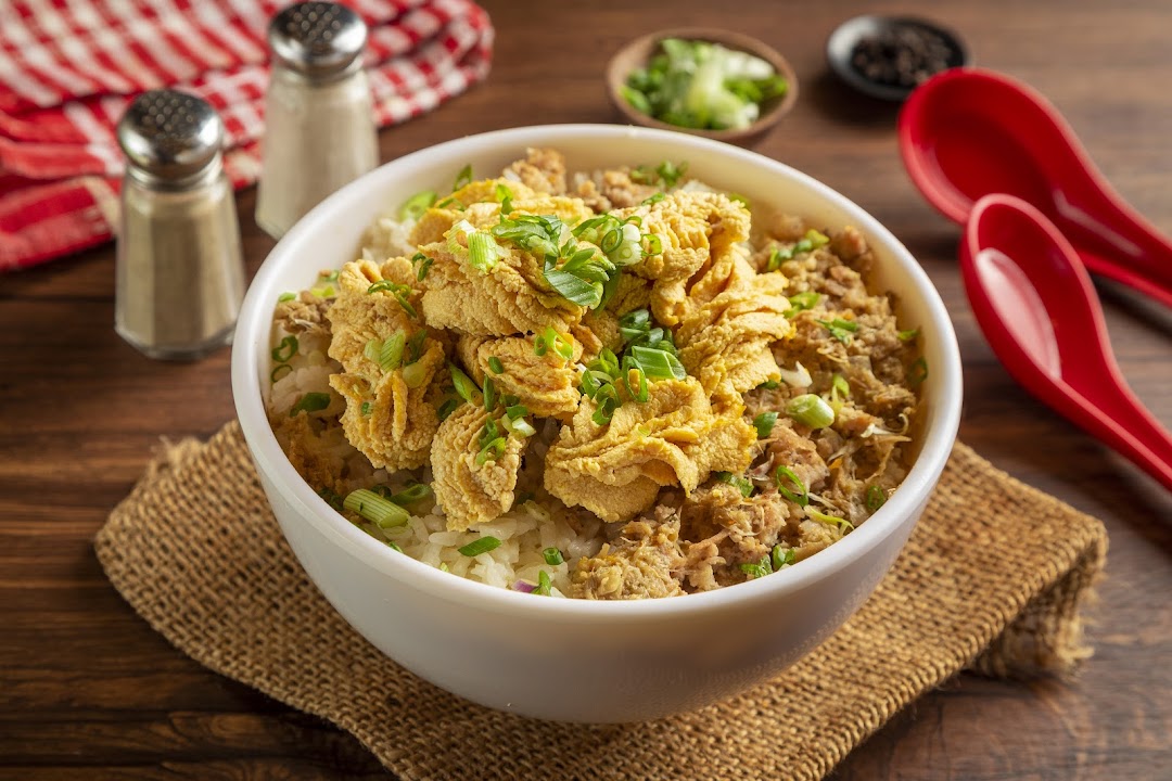 A close-up of a hearty bowl of rice topped with crispy fried items, shredded meat, and fresh spring onions.