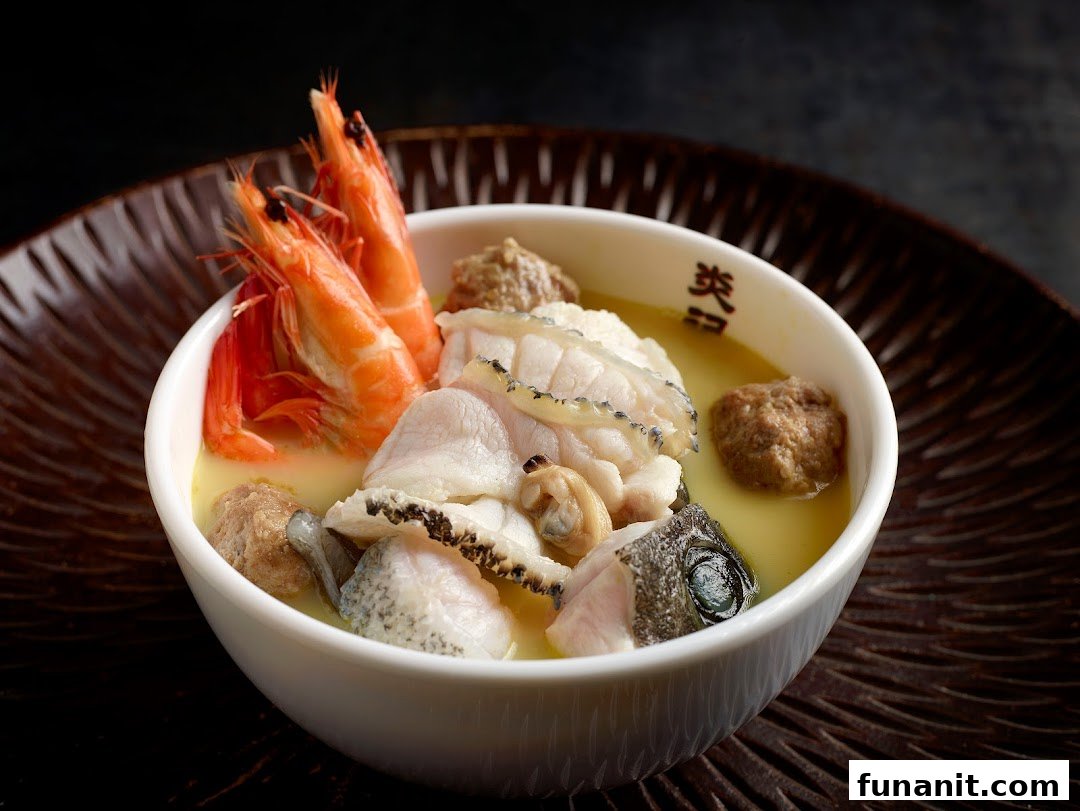 A close-up of a rich seafood soup with prawns, fish, and meatballs in a white bowl.